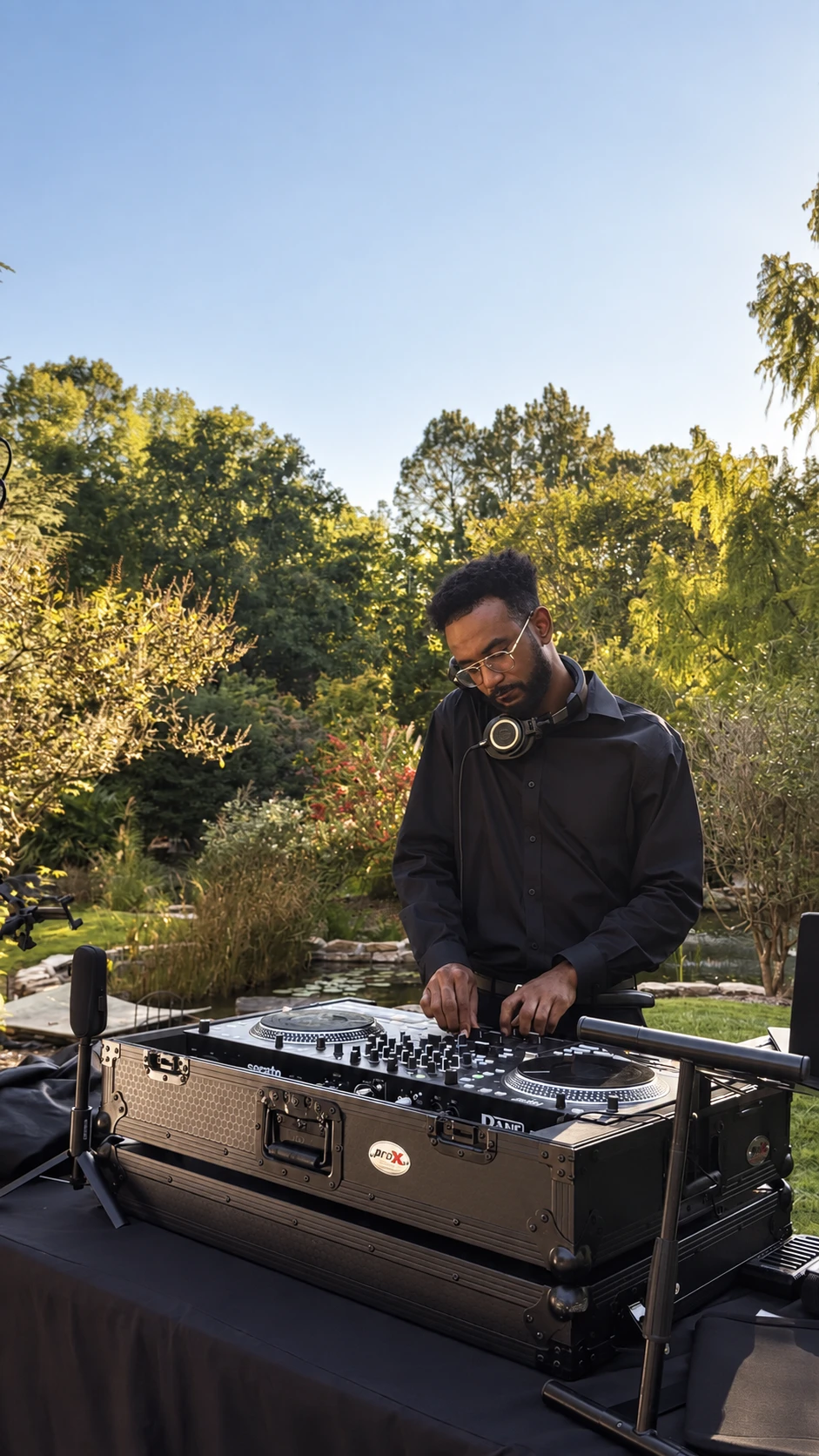 DJ IQ performing at his controller beside a garden pond during an outdoor wedding